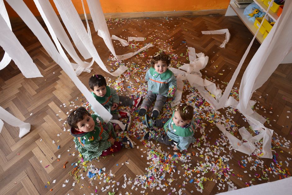 Four children playing indoors with confetti and streamers at a festive party.
