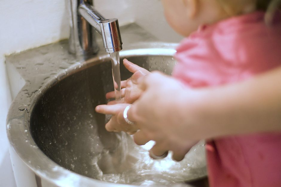 Close-up of a child washing hands with an adult's help under running water in a sink.